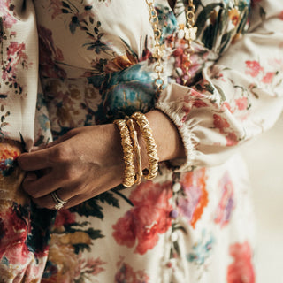Close-up of a hand wearing gold bracelets with a floral dress in the background