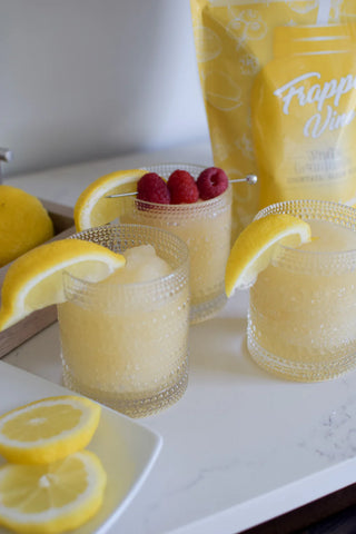 Two glasses of lemonade with raspberries and lemon slices, next to a bag labeled 'Frappuccino Mix'.