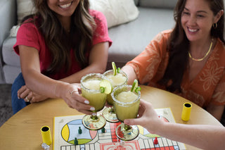 Two women enjoying drinks together at a table with a board game in the background.