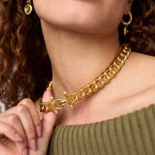 Gold chain necklace worn by a person with green earrings.