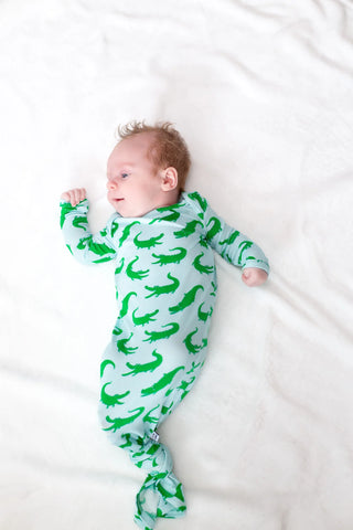 Baby wearing a green alligator patterned onesie on a white background