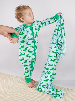 Child wearing a green and white alligator-patterned onesie with a matching blanket.