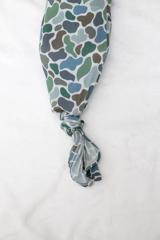 A baby long-sleeve footed sleeper with a green, blue, and brown organic pattern, featuring a knotted ankle and a small side tag, laid flat on a white background.