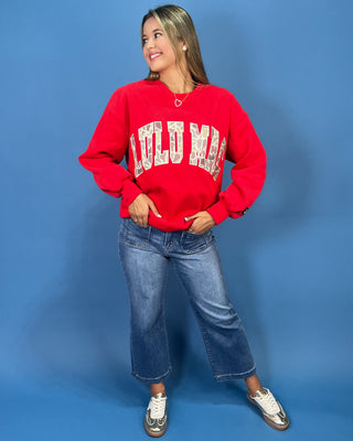 A woman modeling a bright red crewneck sweatshirt with 'LULU MAC' printed in white varsity-style letters