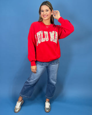 A woman modeling a bright red crewneck sweatshirt with 'LULU MAC' printed in white varsity-style letters