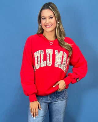 A woman modeling a bright red crewneck sweatshirt with 'LULU MAC' printed in white varsity-style letters
