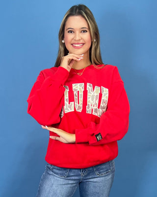 A woman modeling a bright red crewneck sweatshirt with 'LULU MAC' printed in white varsity-style letters