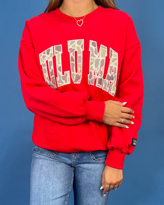 A woman modeling a bright red crewneck sweatshirt with 'LULU MAC' printed in white varsity-style letters