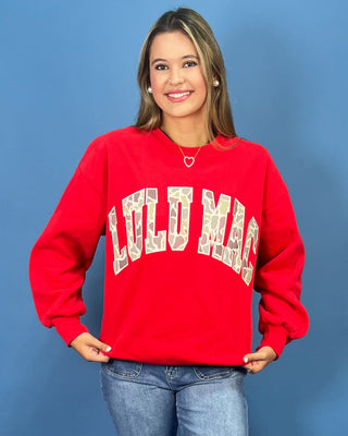 A woman modeling a bright red crewneck sweatshirt with 'LULU MAC' printed in white varsity-style letters