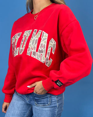 A woman modeling a bright red crewneck sweatshirt with 'LULU MAC' printed in white varsity-style letters