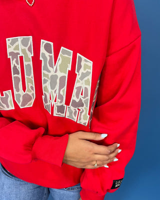 A woman modeling a bright red crewneck sweatshirt with 'LULU MAC' printed in white varsity-style letters