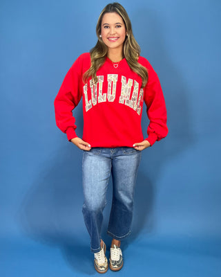 A woman modeling a bright red crewneck sweatshirt with 'LULU MAC' printed in white varsity-style letters