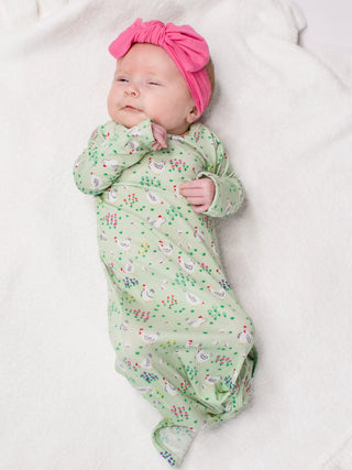 Newborn baby wrapped in a green floral swaddle with a pink headband on a white background