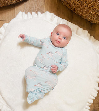Baby wrapped in a light blue swaddle with animal prints on a white blanket.