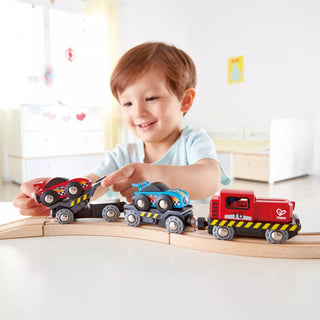 Child playing with toy trains on a wooden track in a bright room.