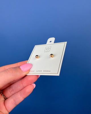 eNewton Classic Gold Ball Stud Earrings featuring polished gold-filled ball studs with secure post backs, minimalist everyday earrings shown on a jewelry card and worn in an ear piercing.