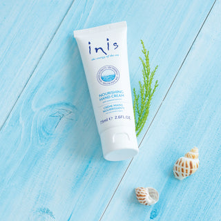 Tube of 'inis' hand cream on a blue wooden surface with greenery and shells.