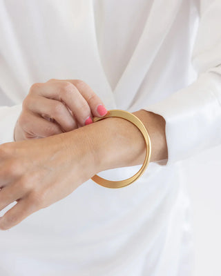Gold bracelet on a wrist with a white background