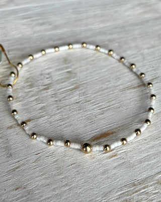 Bracelet with gold and white beads on a light wooden surface