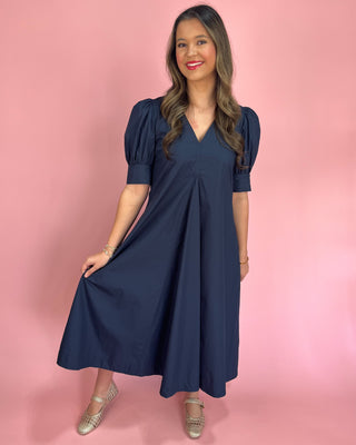 Woman wearing a navy blue dress against a pink background