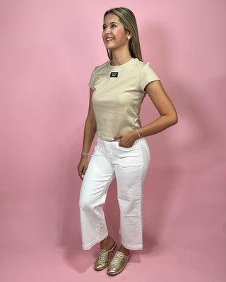 Woman wearing a beige t-shirt and white pants against a pink background