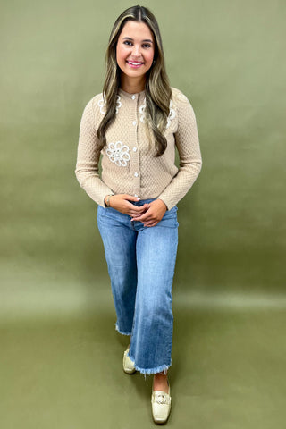 Woman wearing a beige cardigan and blue jeans against a green background