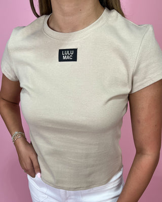 Person wearing a beige t-shirt with 'LULU MAC' logo on a pink background
