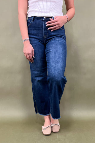 Person wearing blue jeans and a white top against a plain background