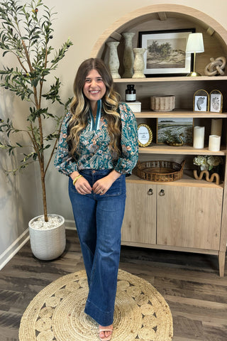 Woman standing in a room with a wooden shelf and decorative items.