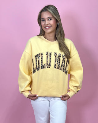 Woman wearing a yellow sweatshirt with leopard print text against a pink background