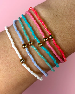 Three beaded bracelets in white, blue, and pink on a wrist against a pink background