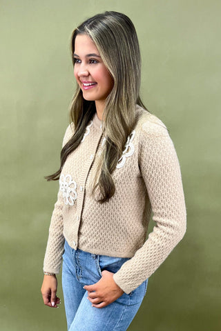 Woman wearing a beige knitted cardigan with floral details on a green background