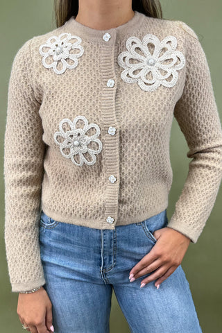 Beige cardigan with floral embellishments worn by a person against a green background
