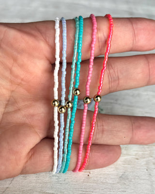 Three colorful beaded bracelets with gold beads on a hand against a neutral background