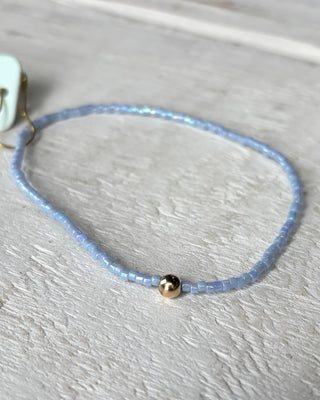 Delicate blue beaded bracelet with a gold accent on a light wooden surface