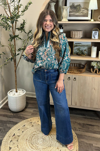 Woman in a floral blouse and blue jeans standing in a living room.