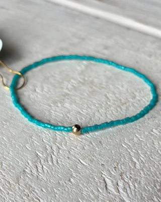Turquoise beaded bracelet with a gold charm on a light gray surface