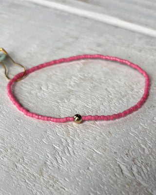 Pink beaded bracelet with a gold clasp on a light gray surface