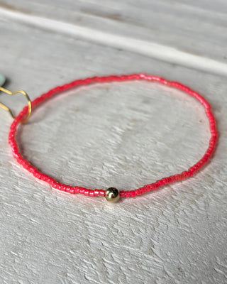 Red string bracelet with a gold bead on a light wooden surface
