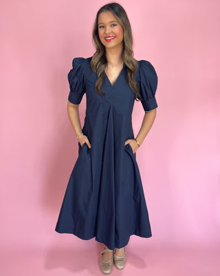 Woman wearing a navy blue dress against a pink background