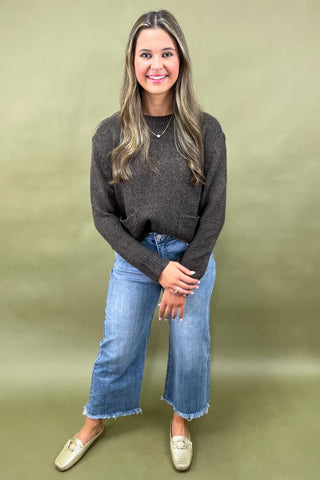 Dark brown cozy knit sweater with front pockets paired with light wash wide leg frayed hem jeans and gold loafers