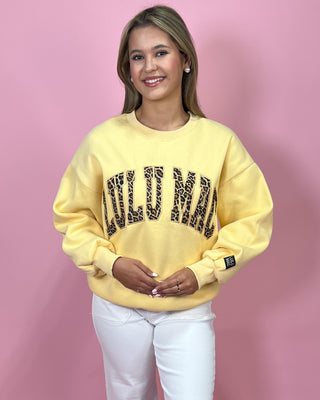 Woman wearing a yellow sweatshirt with leopard print text on a pink background