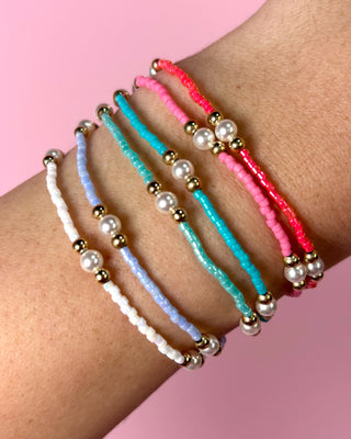 Three beaded bracelets on a wrist against a pink background