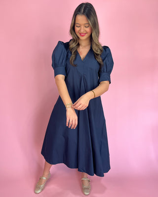 Woman wearing a navy blue dress against a pink background