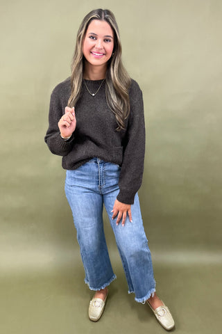 Dark brown cozy knit sweater with front pockets paired with light wash wide leg frayed hem jeans and gold loafers