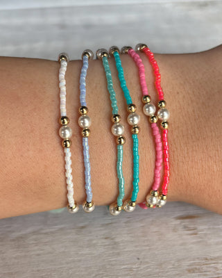 Set of five beaded bracelets on a wrist with a neutral background