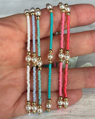 Set of beaded bracelets with pearls and gold beads on a hand.