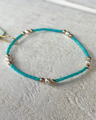 Turquoise bracelet with gold and silver beads on a light gray surface