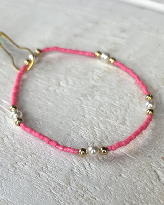 Pink beaded bracelet with gold and pearl accents on a light gray background