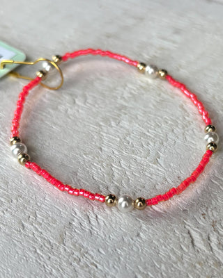 Bracelet with pink cord and gold and silver beads on a light gray background